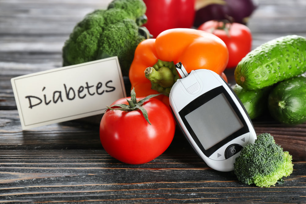 A blood glucose meter rests among fresh vegetables like tomatoes, broccoli, and bell peppers, with a sign reading "Diabetes" in a rustic wooden setting, emphasizing healthy lifestyle choices for diabetes management.