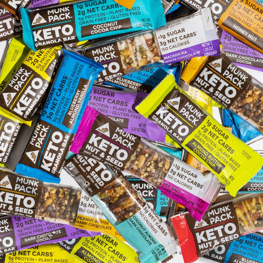 A colorful assortment of Munk Pack keto granola and nut bars is displayed, showcasing various flavors and nutritional information on the packaging, set against a neutral background.