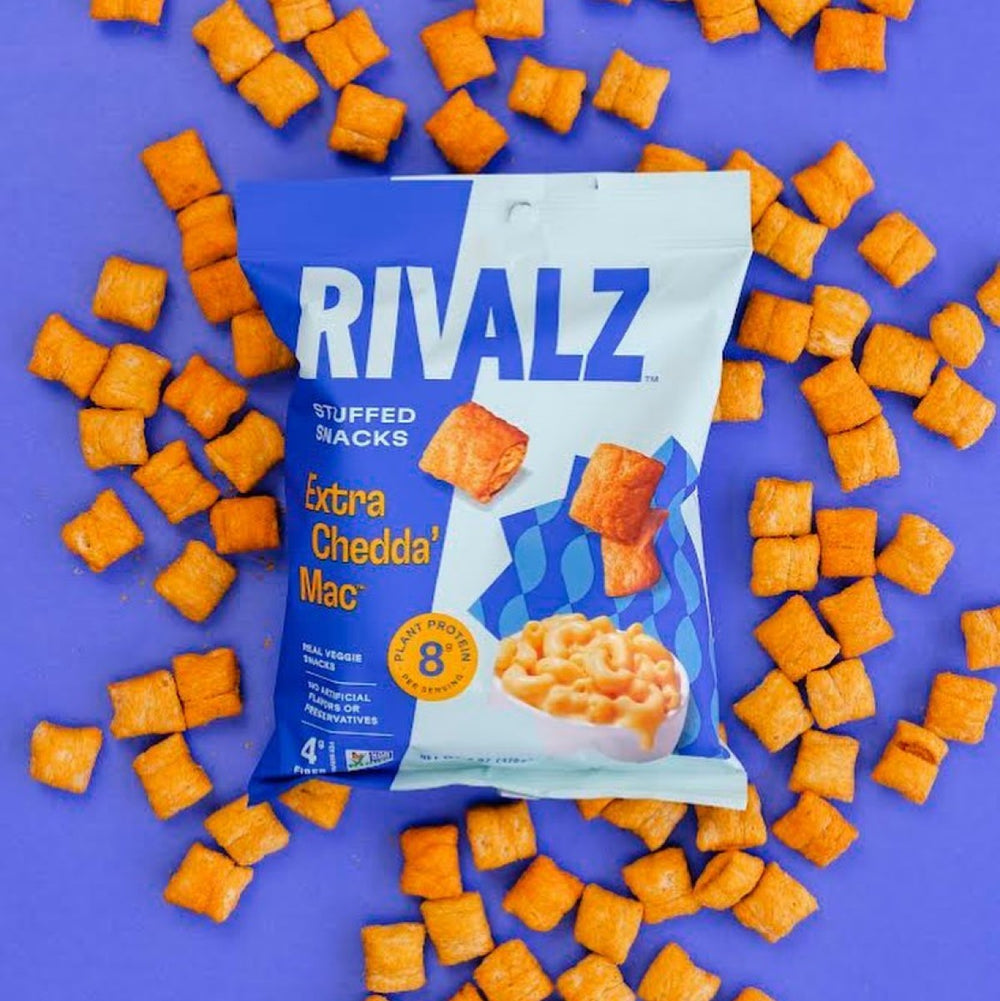 A bag of Rivalz Extra Chedda' Mac stuffed snacks is displayed on a vibrant purple background, surrounded by scattered orange snack pieces, highlighting the product's playful and colorful branding.