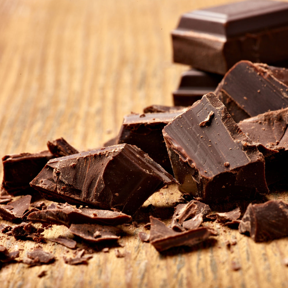 Chunks of dark chocolate are scattered on a wooden surface, with some pieces broken and others intact, showcasing their rich texture and deep color.