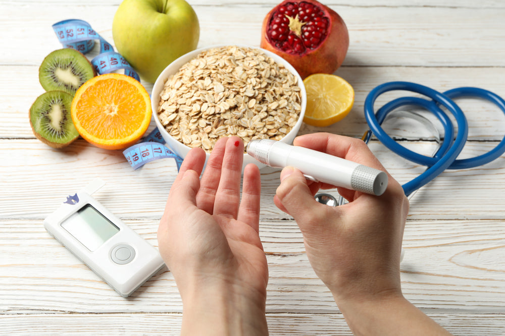 A person is using a blood glucose monitor on their fingertip, surrounded by healthy foods like fruits and oats, along with a measuring tape and a stethoscope on a wooden surface.