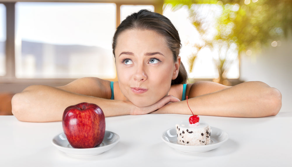 A woman with a thoughtful expression rests her chin on her hands, looking at an apple on one side and a dessert with a cherry on the other, set against a bright, airy background.