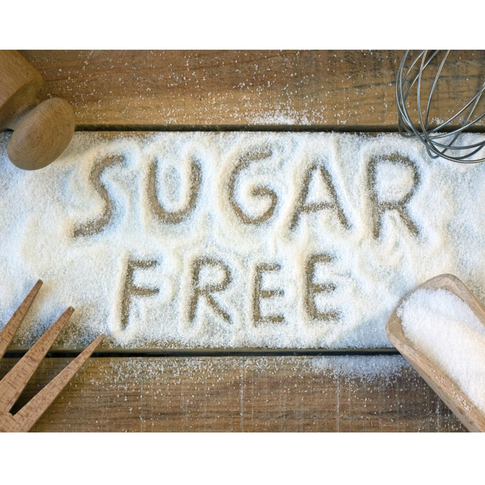 The words "SUGAR FREE" are written in brown sugar on a wooden surface, surrounded by a wooden spoon, a whisk, and measuring tools, emphasizing a healthy cooking theme.