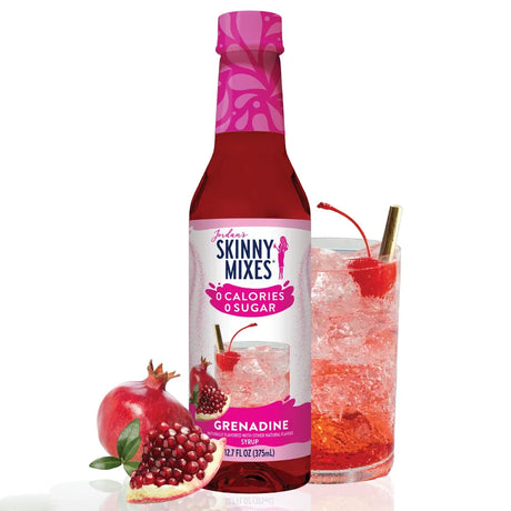 A bottle of Jordan's Skinny Mixes Grenadine syrup stands next to a glass filled with a sparkling drink, garnished with a cherry, alongside a fresh pomegranate cut in half.