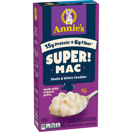 A purple box of Annie's Super Mac featuring shells and white cheddar, highlighting 15 grams of protein and 6 grams of fiber, with a spoonful of creamy pasta shown on the side.