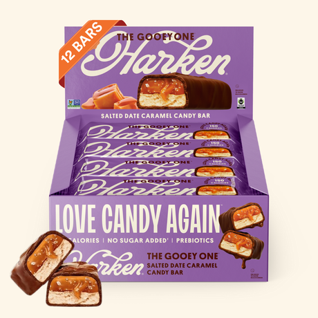 A box of Harken's "The Gooey One" salted date caramel candy bars displays 12 individually wrapped bars, with one cut in half to show the gooey filling, set against a purple background.