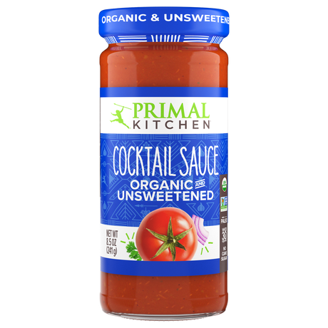 A clear glass jar of Primal Kitchen organic and unsweetened cocktail sauce features a vibrant red sauce with a tomato graphic, labeled prominently in blue and green.