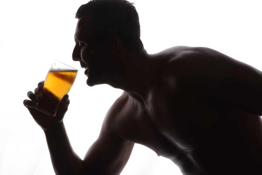 A shirtless man in profile holds a glass of beer, enjoying a drink against a bright, white background that highlights his silhouette.