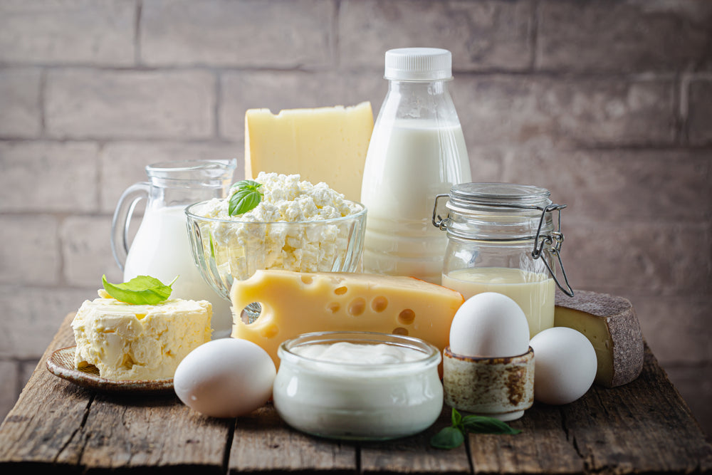A variety of dairy products, including milk, cheese, yogurt, and eggs, are arranged on a wooden table with a rustic background, highlighting options for healthy dairy alternatives.