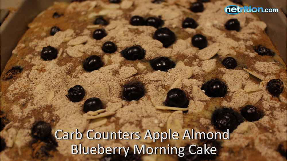 A close-up of a baked apple almond blueberry morning cake topped with whole blueberries and sliced almonds, set in a baking dish.