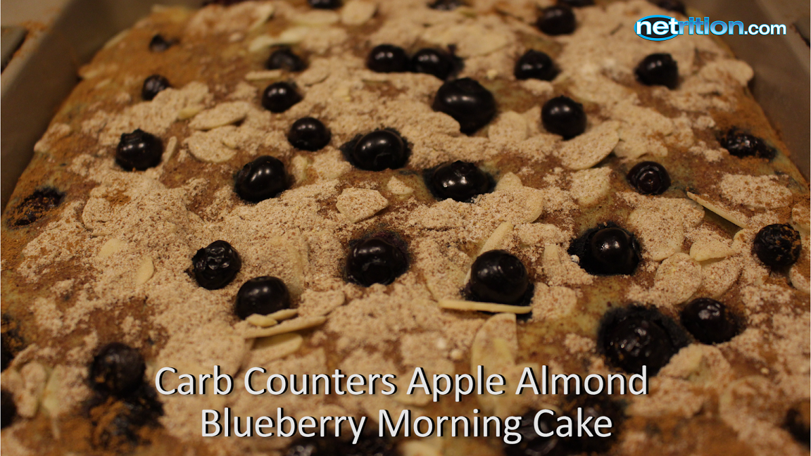 A close-up of a baked apple almond blueberry morning cake topped with whole blueberries and sliced almonds, set in a baking dish.
