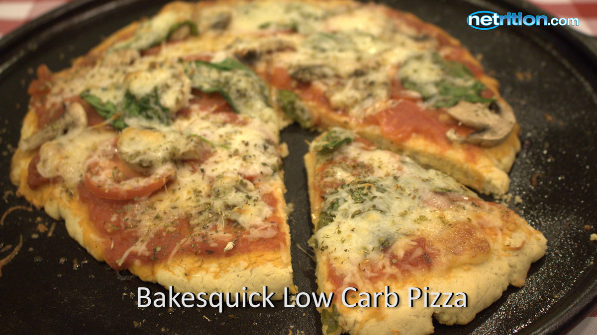 A freshly baked low-carb pizza with melted cheese, sliced tomatoes, mushrooms, and spinach is cut into wedges on a black baking tray.
