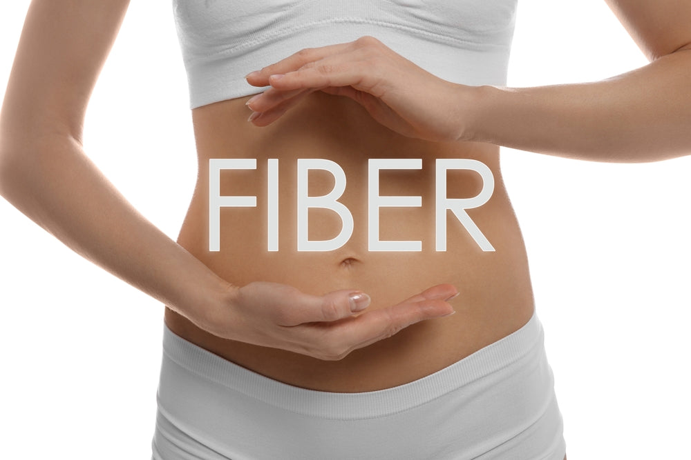 A person in a white top is holding their hands around their midsection, with the word "FIBER" prominently displayed in front, suggesting a focus on health and nutrition.
