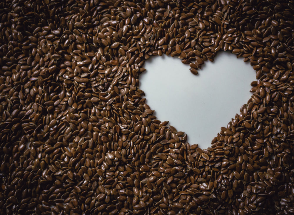 A heart-shaped outline is formed in the center of a bed of brown coffee beans, creating a warm and inviting visual contrast.