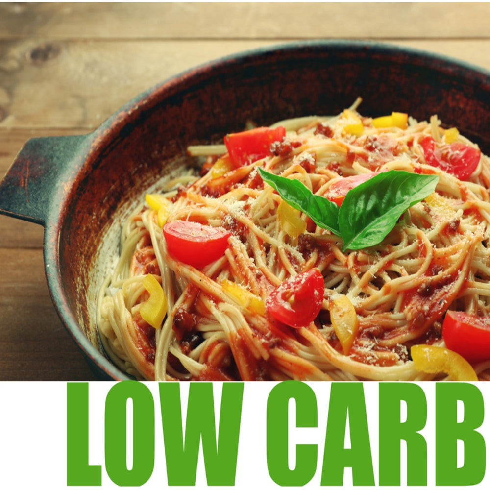 A bowl of low-carb pasta topped with diced tomatoes, yellow peppers, and a fresh basil leaf sits on a wooden table, with the text "LOW CARB" prominently displayed below.