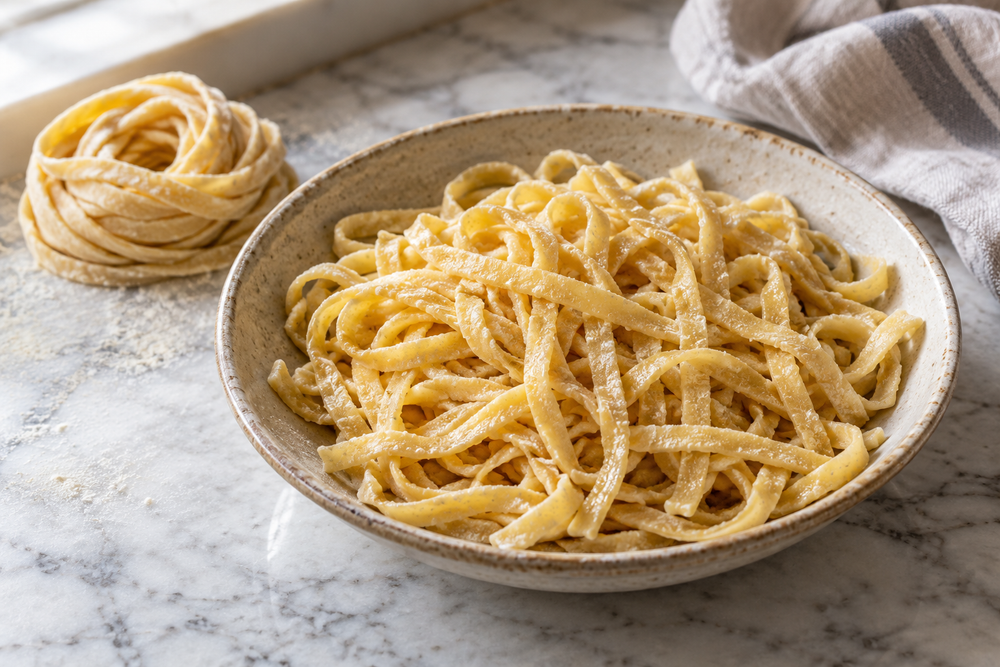 Homemade Carbalose pasta noodles in a bowl beside a coil of uncooked dough.