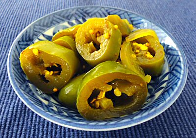 A small blue bowl contains sliced green chili peppers filled with seeds, arranged neatly on a textured blue surface.