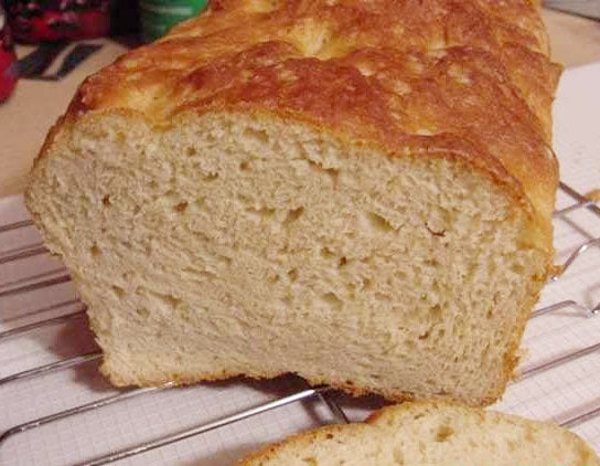 A freshly baked loaf of bread sits on a cooling rack, showcasing a golden-brown crust and a soft, airy interior, with a slice cut off to reveal its fluffy texture.