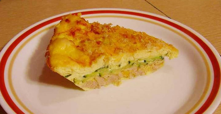 A slice of baked zucchini and tuna casserole is placed on a white plate with a red and yellow rim, showcasing a golden, crispy top and green zucchini layers inside.