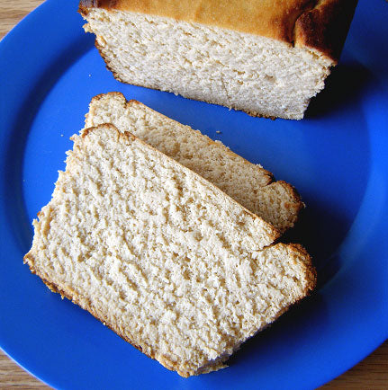 A loaf of freshly baked bread sits on a blue plate, with two slices cut and placed beside it, showcasing its soft texture and golden crust.