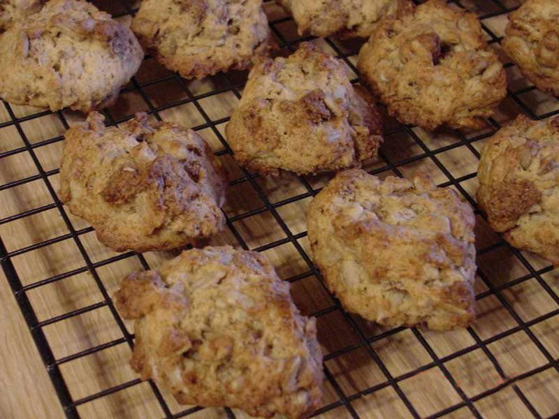 Baked cookies are cooling on a wire rack, showcasing a golden-brown color and a textured surface, with some cookies slightly larger than others.