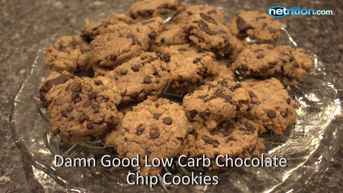 A plate of low-carb chocolate chip cookies is arranged on a glass dish, showcasing their golden-brown color and chocolate chips against a dark granite countertop.