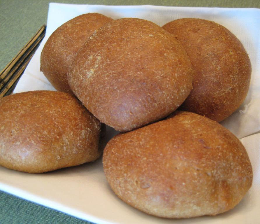 A plate holds five golden-brown, round bread rolls, resting on a white napkin, with a pair of chopsticks placed beside them on a green tablecloth.