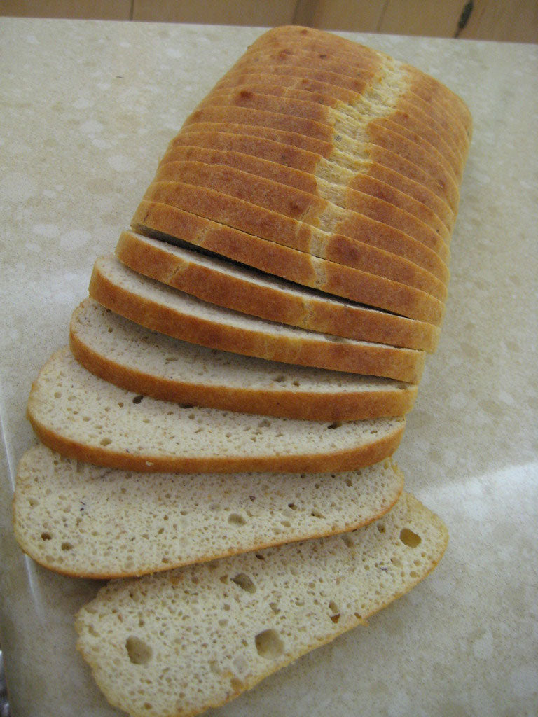 A loaf of sliced bread rests on a countertop, with several evenly cut slices leaning to one side, showcasing its soft texture and light brown crust.