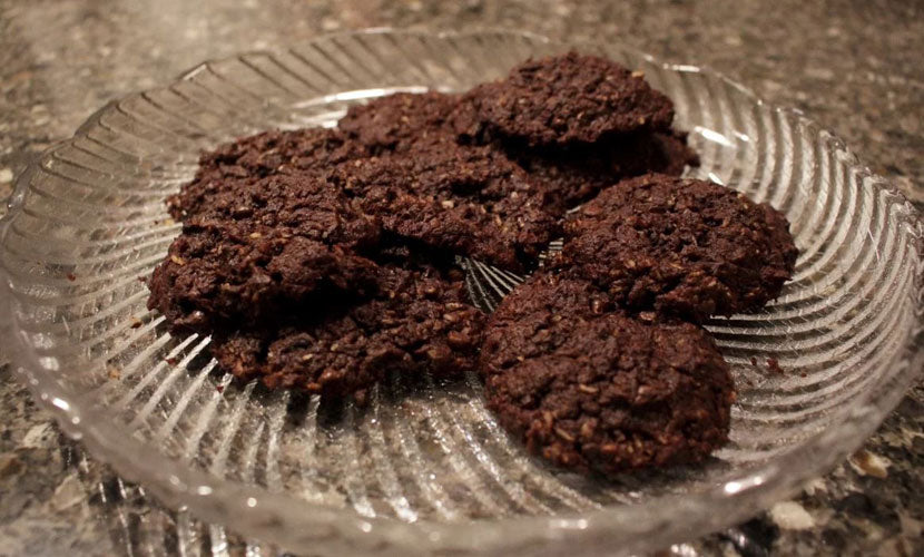 A clear glass plate holds a stack of dark, chewy cookies, showcasing their textured surface, against a dark granite countertop background.