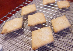Low carb saltines are cooling on a wire rack, displaying a light golden color and a slightly uneven, crisp texture, with several crackers arranged in a casual layout.