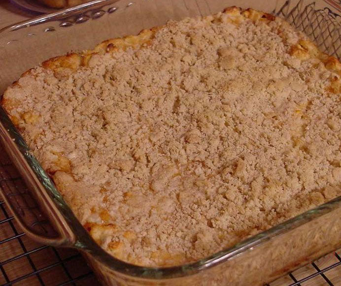 A freshly baked dish with a golden, crumbly topping sits in a glass baking dish on a cooling rack, showcasing its textured surface and inviting aroma.