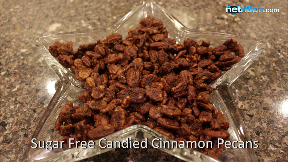 A star-shaped glass dish filled with sugar-free candied cinnamon pecans sits on a dark granite countertop, showcasing the crunchy snack's rich brown color and texture.