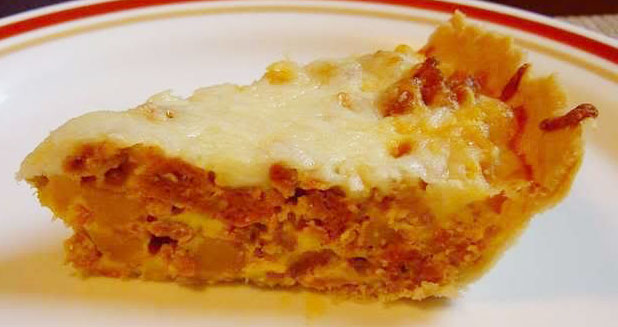 A slice of savory quiche with a golden crust, filled with meat and cheese, sits on a white plate with a red rim, showcasing its layered texture and appetizing appearance.