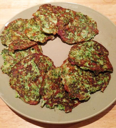 A plate of green vegetable fritters, arranged in a circular pattern, showcases a crispy texture and a vibrant color, set against a wooden table background.