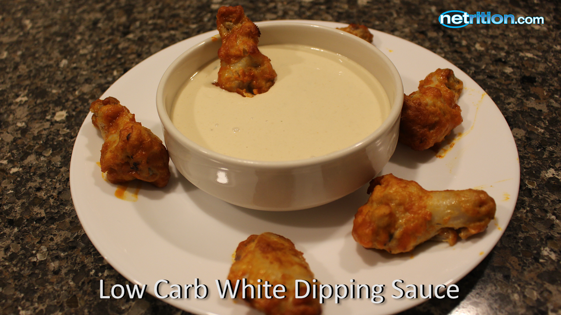 A plate with several crispy chicken wings surrounds a small bowl of creamy white dipping sauce, set on a dark countertop.