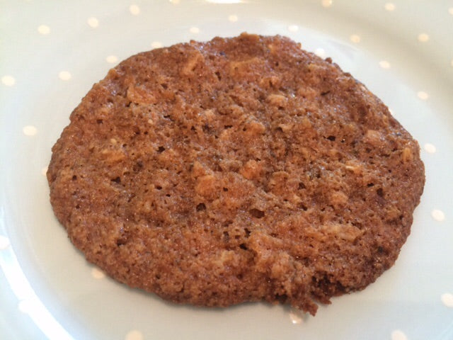 A round, thin cookie with a brown, slightly textured surface sits on a white plate decorated with small polka dots.