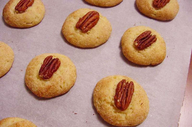 Golden-brown cookies are arranged on parchment paper, each topped with a whole pecan, showcasing a delicious baked treat ready for serving.
