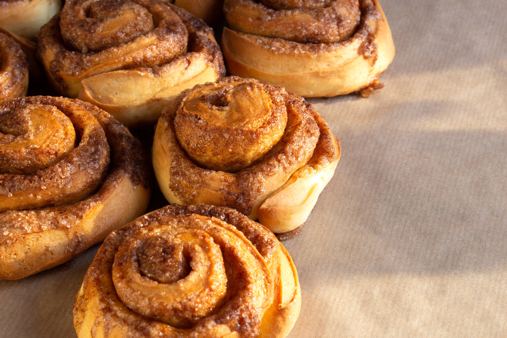 Freshly baked low carb cinnamon rolls are arranged closely on a sheet of parchment paper, showcasing their golden-brown swirls and a dusting of cinnamon sugar on top.