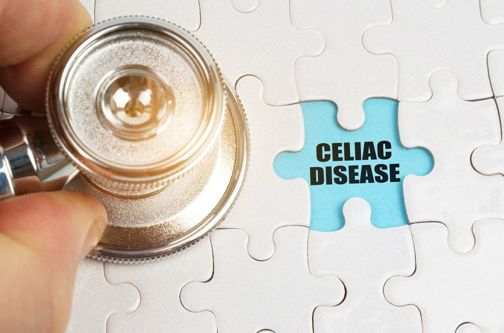 A hand holds a stethoscope above a puzzle piece that reads "CELIAC DISEASE," symbolizing the connection between health and understanding this condition.