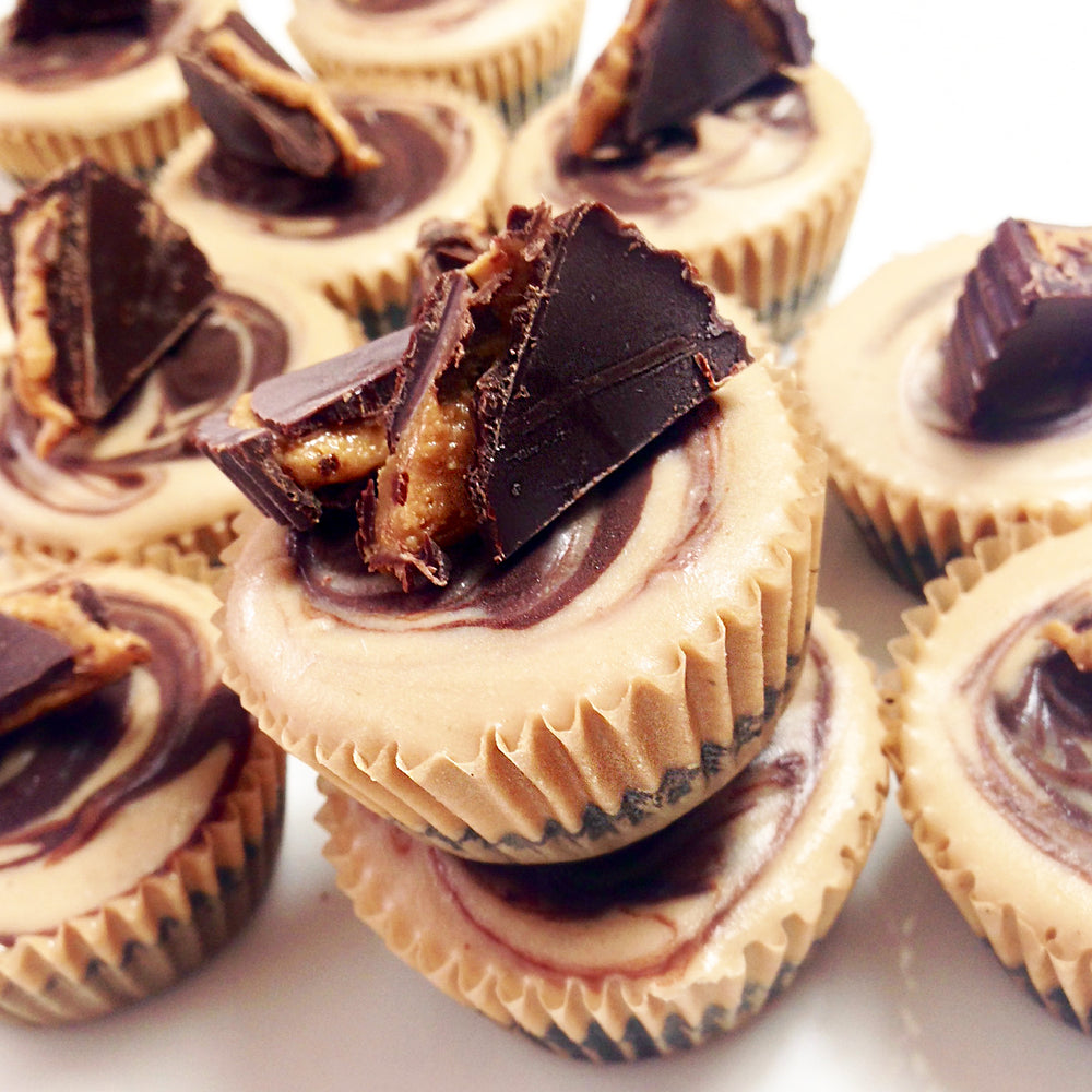 A stack of creamy peanut butter cups topped with chocolate pieces, surrounded by more cups with swirled chocolate and peanut butter, sits on a white surface.