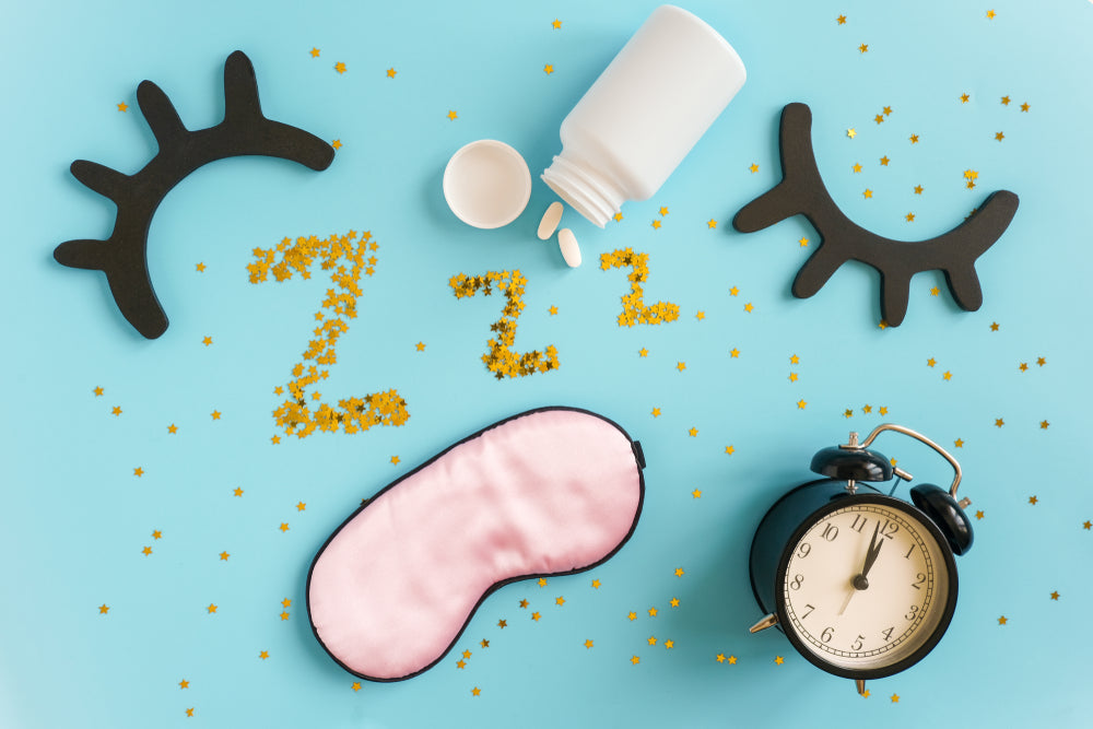 A flat lay features a pink sleep mask, a black alarm clock, a white pill bottle, and decorative stars, with the letters "Zzz" made from yellow glitter, emphasizing the importance of sleep for health.