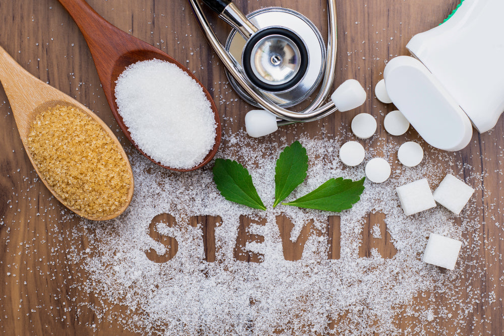 Brown and white sugar, sweetener tablets, and green stevia leaves are arranged on a wooden surface, with the word "STEVIA" formed from white sugar, alongside a stethoscope symbolizing health.