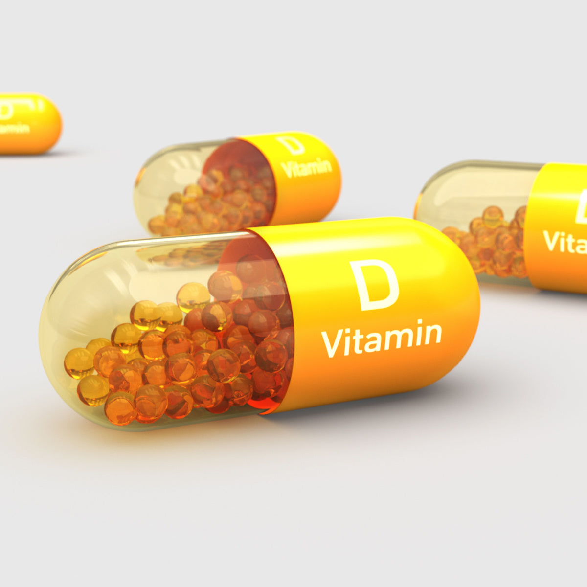 Yellow and transparent capsules filled with orange beads are scattered on a light gray surface, labeled with "Vitamin D," highlighting the importance of vitamin D supplementation.
