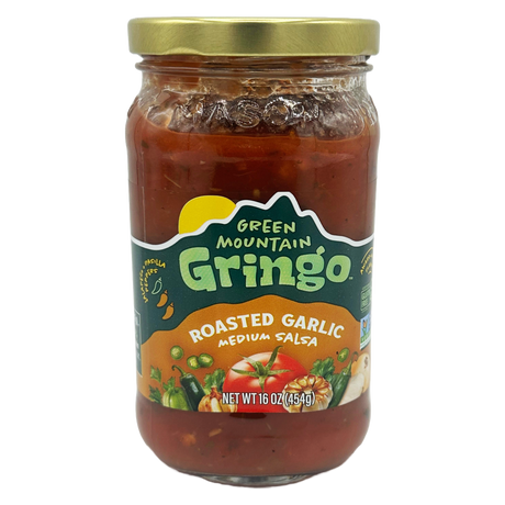A clear glass jar of Green Mountain Gringo roasted garlic medium salsa, featuring a colorful label with images of vegetables, sits against a plain background.