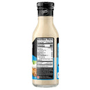 A clear bottle of zero-sugar salad dressing displays nutrition facts and serving information on a black and blue label, with a creamy beige dressing visible inside.