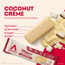 A coconut crème protein bar is displayed next to a creamy coconut sauce and coconut flakes, with nutritional information highlighting 13g protein, 2g net carbs, 1g sugar, and 7g fiber.