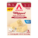 A box of Atkins Whipped high protein bars in Coconut Crème flavor, featuring two bars partially unwrapped to show the filling, with nutritional highlights and a coconut garnish displayed on the side.