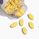 A clear bottle spills yellow oval vitamins onto a white surface, showcasing the product's vibrant color and shape.