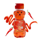 A bear-shaped bottle of ChocZero Hot Honey, with a vibrant orange color, is surrounded by a swirl of honey and a red chili pepper, emphasizing its spicy flavor and vegan ingredients.