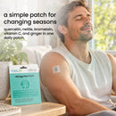 A man relaxes on a couch with a smile, wearing a patch on his arm, while a box of Allergy Plus Patch sits on the table, promoting relief from seasonal allergies with natural ingredients.